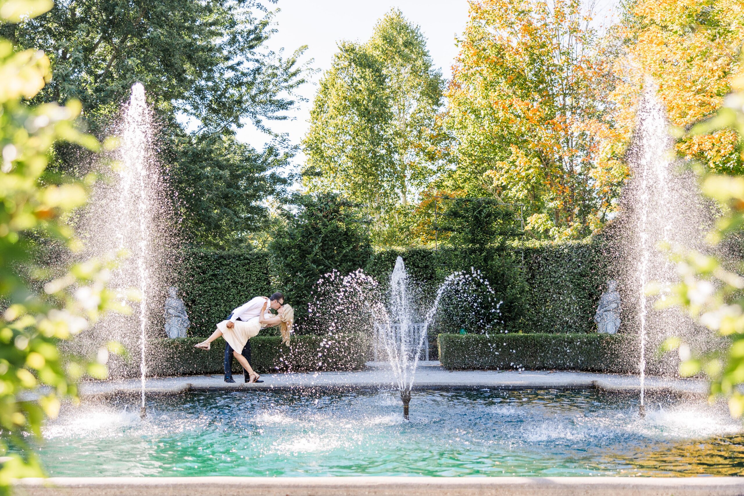 Couple sharing a dip kiss in front of the fountain at the Guelph Arboretum during their summer engagement session, photographed by Kitchener-Waterloo wedding and engagement photographer Alexia Cina.