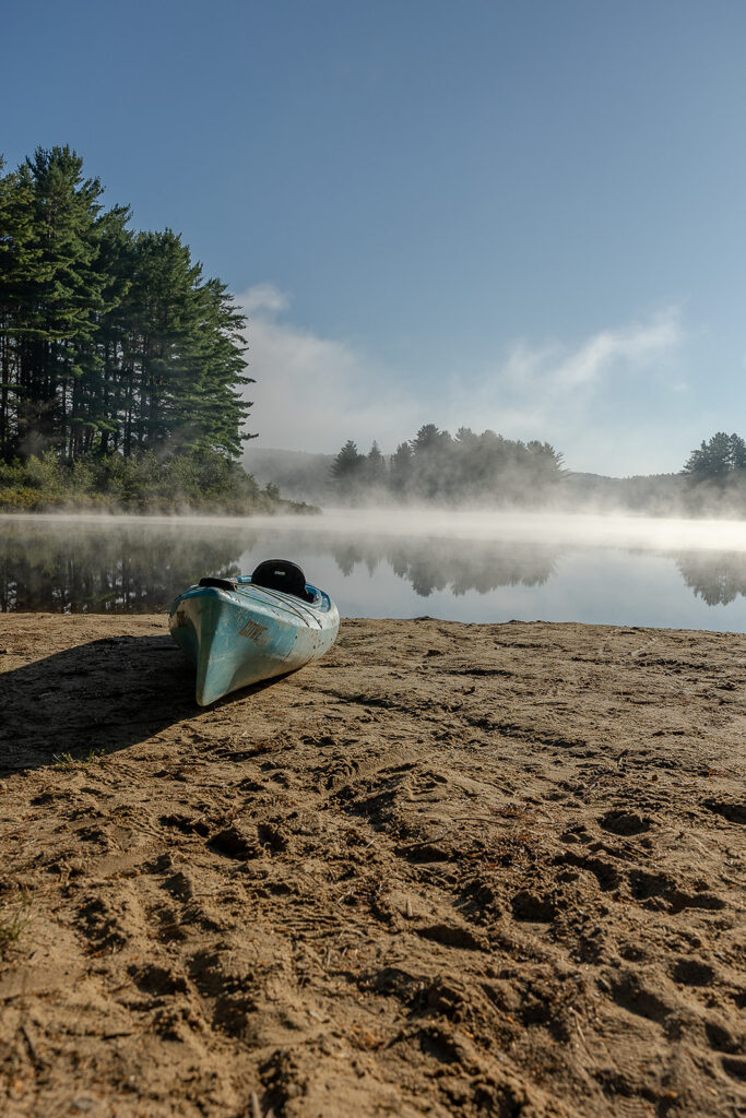 Kayak on the sandy shore of a lake in Algonquin Provincial Park with morning mist over the water.